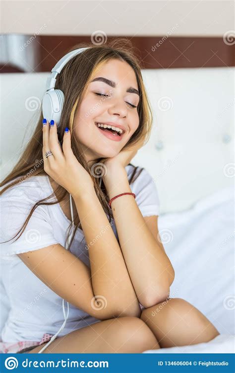 Young Pretty Woman Listening To Music In Headphones On Bed Stock Photo