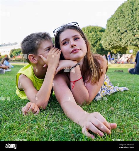 A Young Guy Whispers In The Ear Of A Girl On A Green Lawn Stock Photo