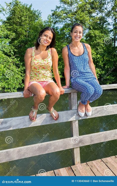 Two Women Sit Together On Bridge Railing Stock Photo Cartoondealer