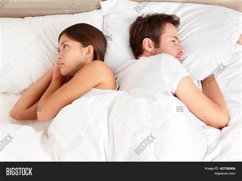 Upset Young Couple Having Marital Problems Or A Disagreement Lying Side By Side In Bed Facing In