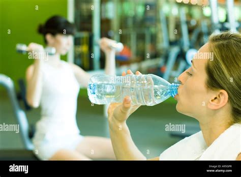 Two Women In Weight Room Focus On Woman In Foreground Drinking Bottle