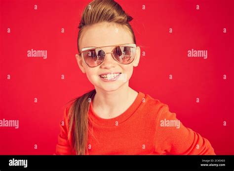 Portrait Of Brunette Girl Wearing Red T Shirt And Sunglasses On Red Background Looking At