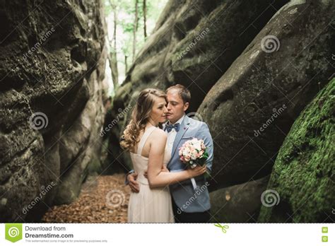 Gorgeous Wedding Couple Kissing And Hugging In Forest With Big Rocks