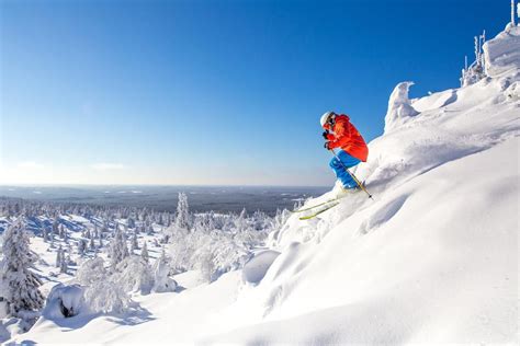 A Man Riding Skis Down The Side Of A Snow Covered Slope Next To Trees