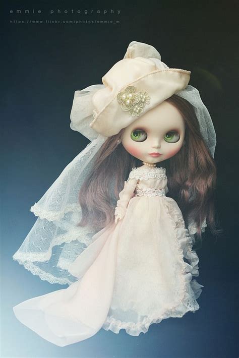 A Doll Is Wearing A White Dress And Hat With Pearls On Its Head