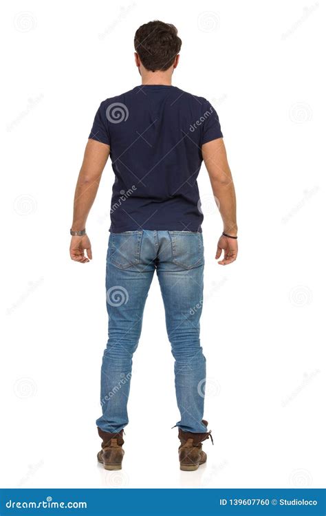 Young Man In Jeans And Blue T Shirt Is Standing Relaxed Rear View