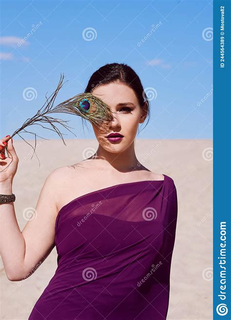 amazing beautiful brunette woman with the peacock feather in purple fabric in the desert stock