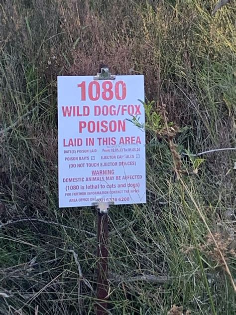 A White Sign With Red Text Stating That 1080 Wild Dog And Fox Poison