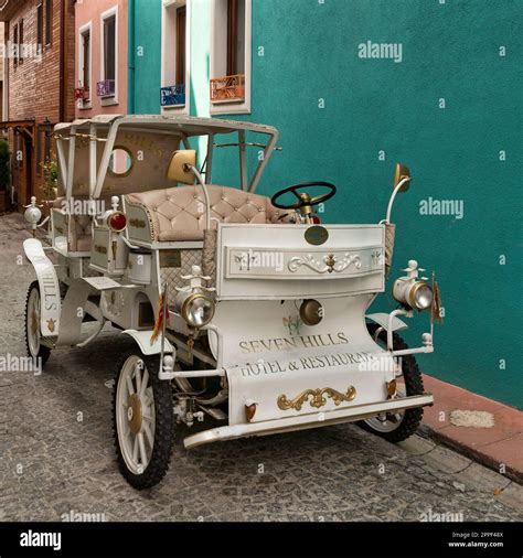 White antique car in a cobblestone alley over green wall of Seven Hills