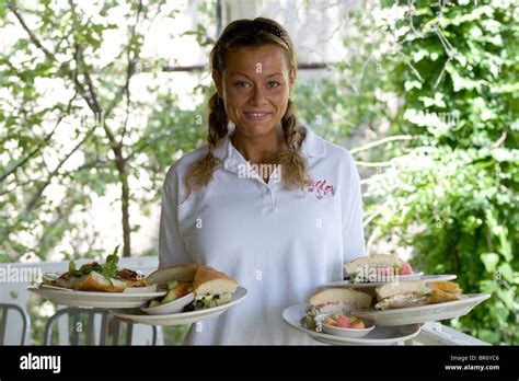 A Waitress Smiles An Holds Out Two Trays With Plates Of Food On Them At
