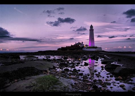 A Purple Light House Sitting On Top Of A Rocky Beach