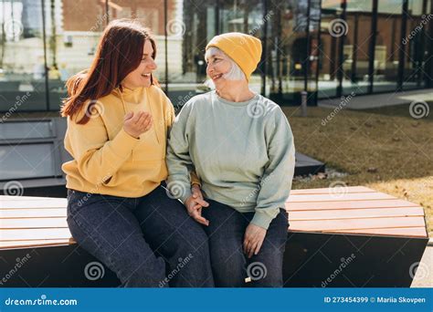 Two Womans Sitting Outside On A Bench And Talking Along On City Street