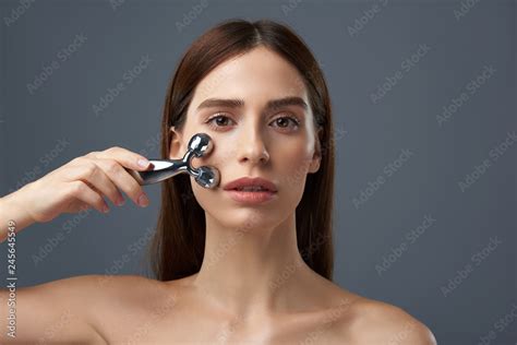 Gorgeous Brunette Girl With Naked Shoulders Using Facial Massager Stock Photo Adobe Stock