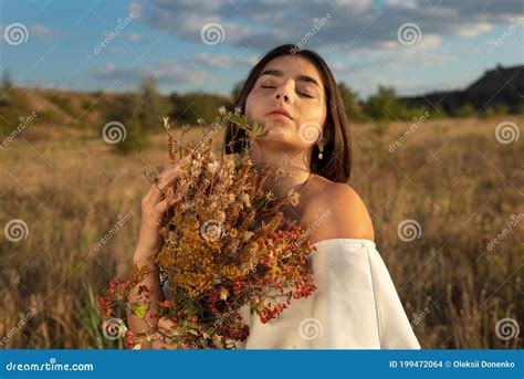 Portrait Of A Young Beautiful Brunette Girl In A White Dress Holding A Bouquet Of Wildflowers