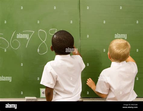 Young African And Caucasian Boys Writing On A Classroom Blackboard