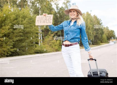 Smiling Confident Experienced Glad Blond Woman In Hat Hitchhiking With Carton Board Anywhere