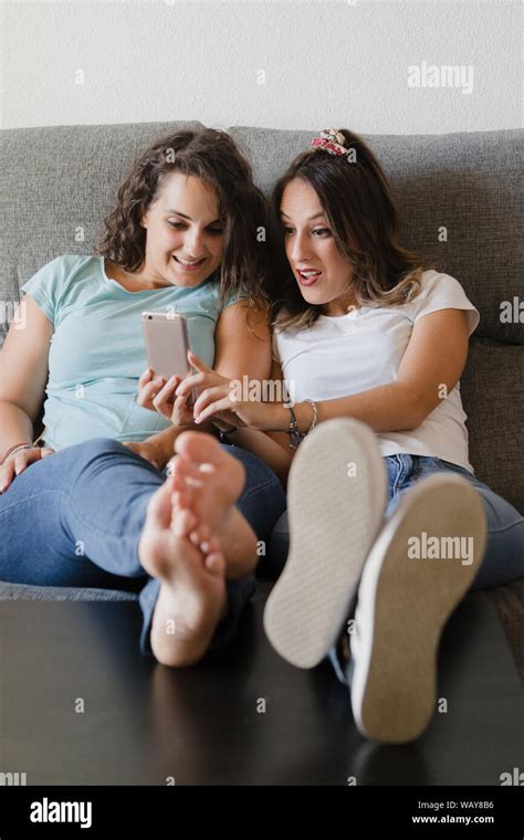 Girls In A Couch With Feet In A Table Looking A Mobile Phone Stock Photo Alamy