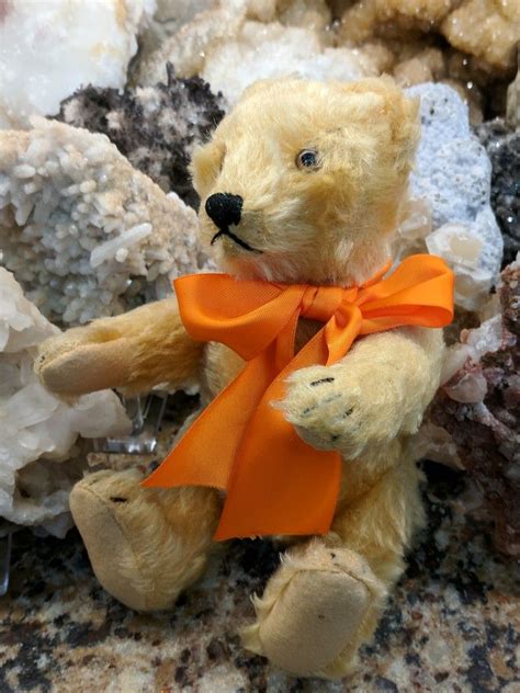 A Teddy Bear With An Orange Ribbon Sitting On Some Rocks