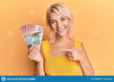 Young Blonde Girl Holding 100 New Zealand Dollars Banknote Smiling