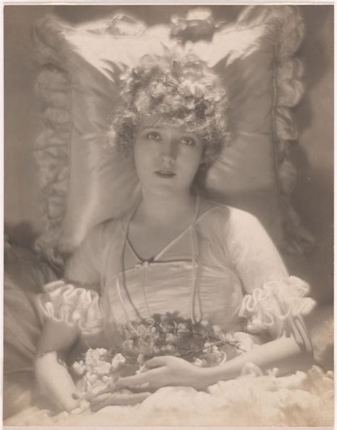 an old black and white photo of a woman with flowers in her hair sitting on a bed