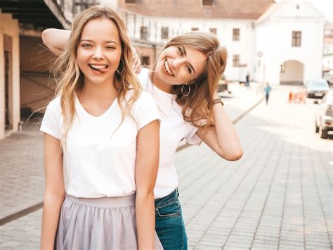 トレンディな夏の白いtシャツ服で流行に敏感な女の子を笑顔2つの若い美しいブロンドの肖像画。 。ポジティブモデルは舌を示しています 無料の写真