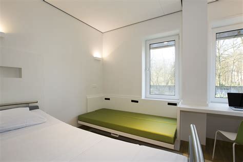 A Room With A Bed Desk And Two Windows In The Same Area That Is White