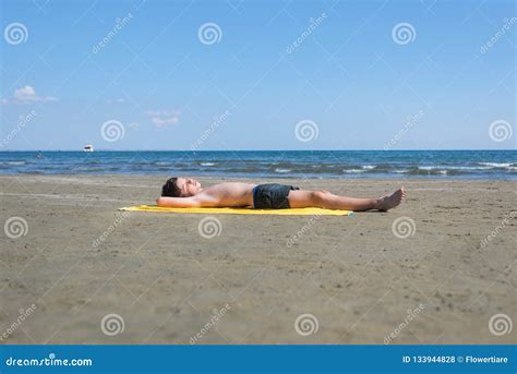 Teen Boy Lies On Yellow Towel And Sunbathes On The Beach Traveling On
