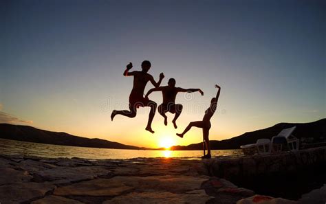 Silhouette Of Friends Jumping At Sunset On The Beach Stock Photo