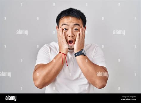 Young Chinese Man Standing Over White Background Afraid And Shocked