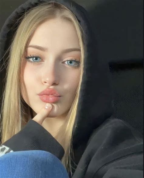 a woman with long blonde hair and blue eyes wearing a black hoodie looking at the camera