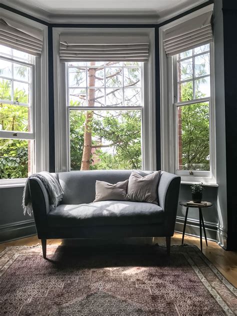 In this living room, a pair of windows and a set of french doors are dressed in identical curtains mounted just below the ceiling. Dark Living Room #romanblinds (2020) | Bay window living ...