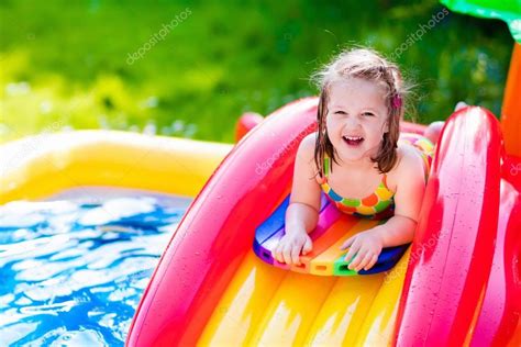 Маленькая девочка играет в надувной бассейн сад стоковое фото
