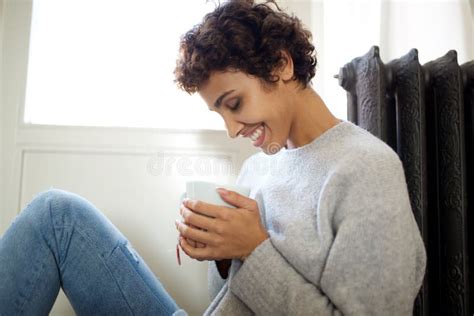 Relaxed Young Woman Sitting On Floor Against Radiator Heater With Cup