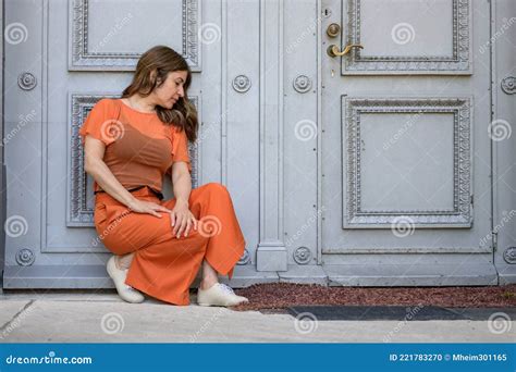 Dejected Woman Crouching Against A Historic Wooden Door Waiting Stock