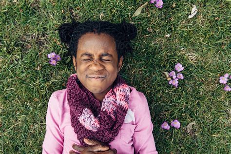 silly black girl with closed eyes laying on grass with crocus flowers by stocksy contributor