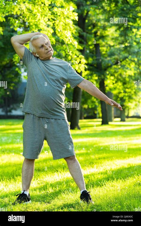 Active Elderly Man Exercising In Green City Park During His Fitness