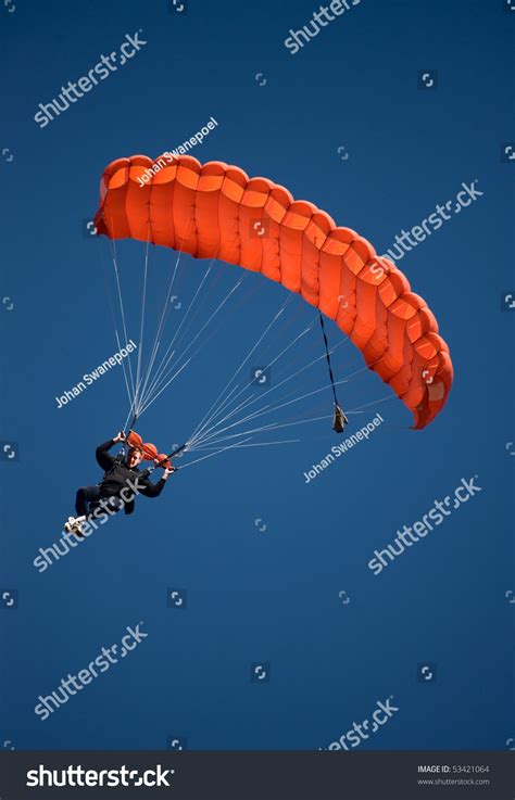 Parachuter Descending With A Red Parachute Against Blue Sky Stock Photo