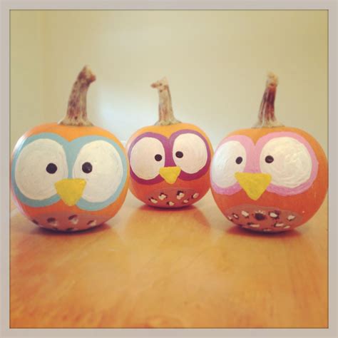 Three Painted Pumpkins With Owls And Giraffe Faces Sitting On A Wooden
