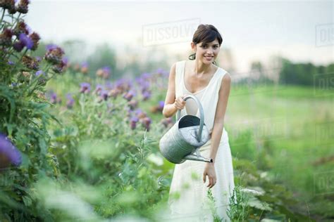 Young Woman Watering Plants In Garden With Watering Can Smiling At