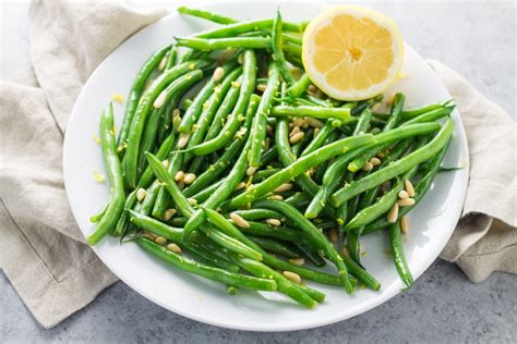 A White Plate Topped With Green Beans And Lemon