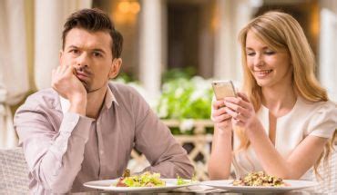 A Man And Woman Sitting At A Table Looking At A Cell Phone While They