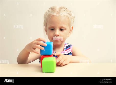 Funny Little Girl Hiding Behind White Table And Taking Colourful Cubes