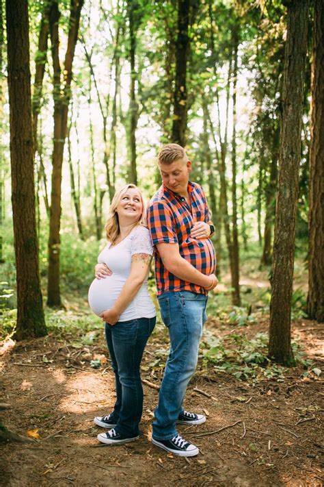 A Pregnant Couple Standing Together In The Woods