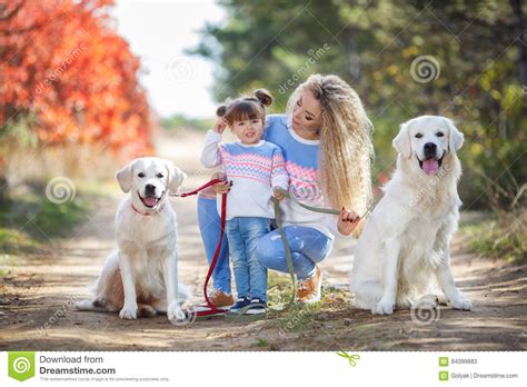 A Young Mother With A Little Girl And Two Dogs On A Walk In The Park In