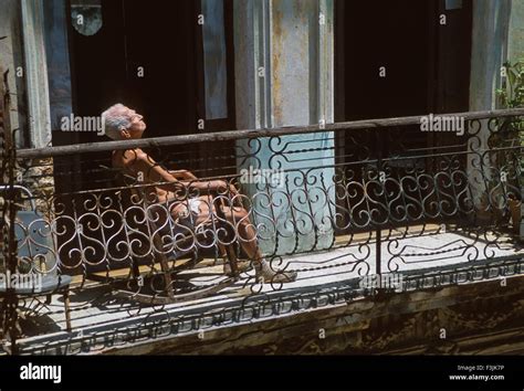 Old Man Sunbathing On A Balcony In A Run Down Street In Centro Habana
