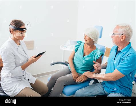 Ent Doctor Talking With Senior Patients In Doctors Office Stock Photo