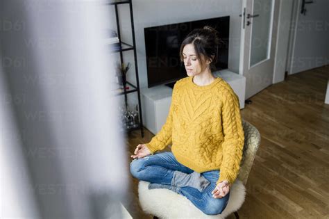 Mature Woman Sitting Cross Legged On Chair With Eyes Closed Meditating