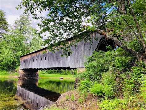 an old covered bridge over a river in the woods with trees and grass around it