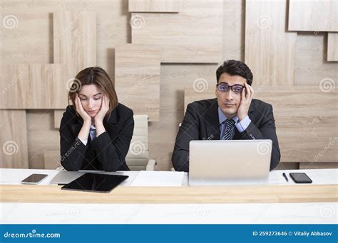 Stressed Male And Female Business Persons Sitting At Desk Hard