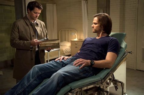 A Man Sitting In A Hospital Bed With Another Man Standing Next To Him